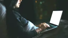 A woman in a dark room on her laptop