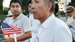 O veterano Alejandro Barranco aparece em foco segurando uma bandeira dos EUA durante vigília em homenagem ao pai, Narciso Barranco, e em protesto contra operações migratórias do governo Donald Trump, em 27 de junho de 2025, em Santa Ana, Califórnia.