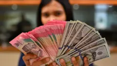 Karyawan memperlihatkan uang pecahan rupiah dan dolar Amerika Serikat (AS) di gerai penukaran mata uang asing Ayu Masagung, Jakarta, Selasa (12/5/2026). 