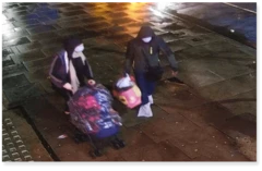 Imagem de câmera de segurança mostra casal de capuz e máscara facial carregando uma sacola e carrinho de bebê