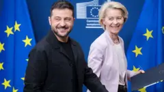 Prezydent Ukrainy Wołodymyr Zełenski (po lewej) i przewodnicząca Komisji Europejskiej Ursula von der Leyen (po prawej) maszerują przed flagami Unii Europejskiej z niebieską i żółtą gwiazdą