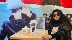 Olive duduk di samping poster Gojo Satoru