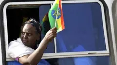 ባንዴራ ሒዛ ብመስኮት ኣውቶቡስ እተቐልቀለት ኣደ