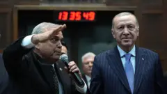 Erdoğan'ın yanındaki eski CHP'li vekil, selam duruyor. Erdoğan ileri bakarak tebessüm ediyor.