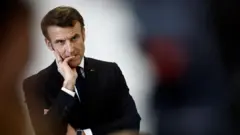 Emmanuel Macron looks at crowd with hand on mouth