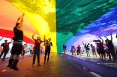 Pessoas embaixo de bandeira arco-íris