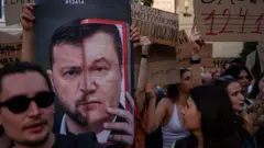 Плакат із зображенням президента Володимира Зеленського та колишнього проросійського президента України Віктора Януковича під час протесту проти законопроекту, що обмежує повноваження антикорупційних органів, 23 липня 2025 року в Києві