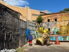 Área aberta com carro alegórico; atrás, prédio construído