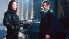 Lucy Liu e Antonio Banderas, ambos vestidos de preto e segurando armas em uma cena de Ballistic: Ecks vs Sever