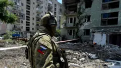Um soldado russo patrulha um bairro residencial destruído na cidade de Severodonetsk, em 12 de julho de 2022, enquanto a ofensiva militar russa continua na Ucrânia.
