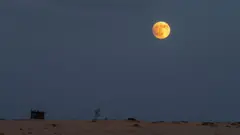 Uma lua vermelha brilhante no alto de um céu nublado e pálido acima de um deserto arenoso