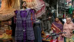Shopkeeper showing a dress while two women are passing by.