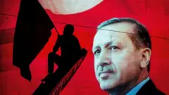 Un partidario del presidente turco Recep Tayyip Erdogan ondea una bandera frente a una pantalla publicitaria electrónica durante un mitin en la plaza Kizilay, el 18 de julio de 2016, en Ankara (Turquía).