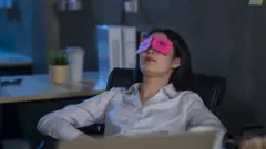 Mulher sentada em cadeira de escritório, reclinada, com papéis em cima seus olhos - indicando que ela está cansada