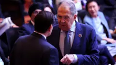 O ministro das Relações Exteriores da Rússia, Sergei Lavrov, aparece de frente para Rubio, com a mão estendida em sua direção, durante a 15ª Reunião de Chanceleres da Cúpula da Ásia Oriental, no Centro de Convenções da capital malaia, Kuala Lumpur, em 11 de julho de 2025. Outros delegados estão sentados ao fundo.