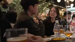 Um homem e uma mulher conversando diante de mesa com comidas e bebidas 