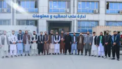 اداره ملی احصائیه و معلومات حکومت طالبان که تعدادی از کارمندان آن در برابر آن عکس گرفته‌اند.