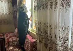 Una mujer afgana cierra las cortinas de su casa