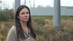 Emily Kasabian se encuentra frente a una subestación con postes gigantes.