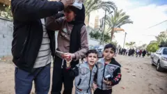 Una mujer herida junto a dos niños en Gaza.