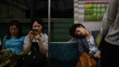 Três pessoas em um vagão de metrô. O homem à direita está dormindo