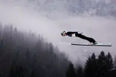 El francés Marco Heinis en un salto, con las montañas de Val di Fiemme de fondo, en Milán-Cortina 2026