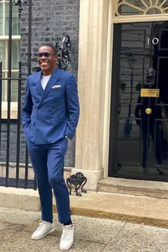 Komolafe em pé em frente ao número 10 da Downing Street, residência oficial e escritório de trabalho do Primeiro-Ministro do Reino Unido.