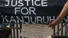 Seorang warga melihat tulisan yang dibawa suporter Arema Malang Miftahuddin Ramly dengan sepedanya usai tiba di Stadion Utama Gelora Bung Karno (SUGBK), Jakarta, Senin (14/8/2023).