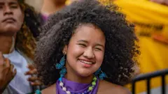 Catalina La Grande tiene el pelo oscuro y rizado. Está sonriendo frente a la multitud y lleva pendientes azules con forma de mariposa.