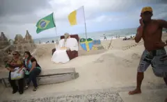 Em Copacabana, em 2013, turistas tiram foto com homenagem a Francisco, que escolheu o Brasil como seu primeiro destino fora da Itália como papa
