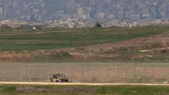 Gazze'nin uzaktan görünümü. Tellerin arkasında enkazlar, önünde bir tank var.