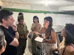 Em garagem, Isabella falando, rodeada por outras pessoas