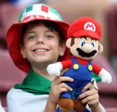 Un joven aficionado de la selección italiana posa para una foto mientras sostiene un muñeco de peluche de Super Mario, disfrutando del ambiente previo al partido de cuartos de final de la Eurocopa Femenina de la UEFA 2025 entre Noruega e Italia, que se disputará el 16 de julio de 2025 en el Estadio de Ginebra, en Ginebra, Suiza.