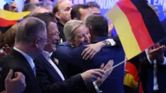 Алис Вайдель обнимается с мужчиной, в руках у нее флаг Германии.