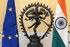 Las banderas de la UE e India flanqueando una pequeña escultura.