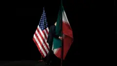 أحد الموظفين يزيل العلم الإيراني من المسرح بعد التقاط صورة جماعية مع وزراء الخارجية وممثلي الولايات المتحدة وإيران والصين وروسيا وبريطانيا وألمانيا وفرنسا والاتحاد الأوروبي خلال المحادثات النووية الإيرانية في مركز فيينا الدولي.