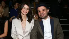 Beren Saat ve Kenan Doğulu yan yana oturuyor. Doğulu bir şapka takıyor.