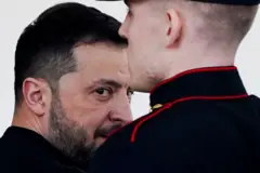 Zelensky com olhar sério, atrás de guarda
