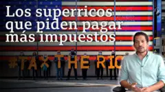 Bandera estadounidense y personas sosteniendo letras que forman la frase "Graven a los ricos"