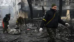 Police officers remove the body of a passerby killed in yesterday's airstrike that hit Kyiv's main television tower in Kyiv on 2 March 2022