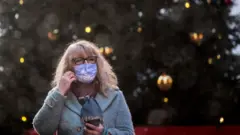 A woman wearing a face mask in front of a Christmas tree in the Leadenhall Market in London.