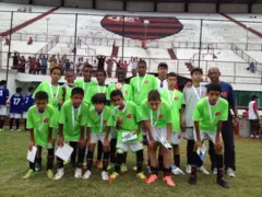 Um grupo de crianças usando uniforme verde. Vini Jr está na fileira de cima