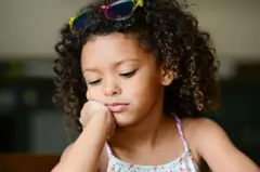 Una niña con la mirada perdida mientras apoya su cara sobre su brazo