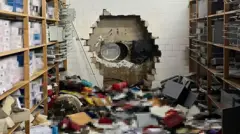 Um buraco enorme em uma parede e várias caixas espalhadas pelo chão