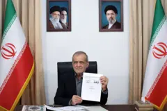 الرئيس الإيراني، مسعود بزشكيان،  يجلس في مكتبه ويمسك أمام الكاميرا  بمذكرة تفاهم تهدف إلى إنهاء الحرب بين إيران والولايات المتحدة، بوساطة باكستانية، تم توقيعها في في 18 يونيو/حزيران، وفي الخلفية علم إيران