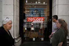 Pessoas caminham diante de um cartaz que anuncia "70% off" em uma loja de Buenos Aires.