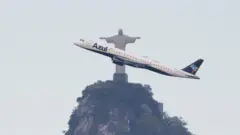 Avião da Azul sobrevoa o Cristo Redentor, no Rio de Janeiro, em imagem que destaca a aeronave passando diante do monumento.