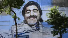 An artist uses a crane to paint a large mural of Maradona on the side of a building