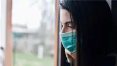 Mulher de máscara olhando pela janela
