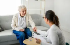 Uma senhora idosa conversa com uma psicóloga em consultório
